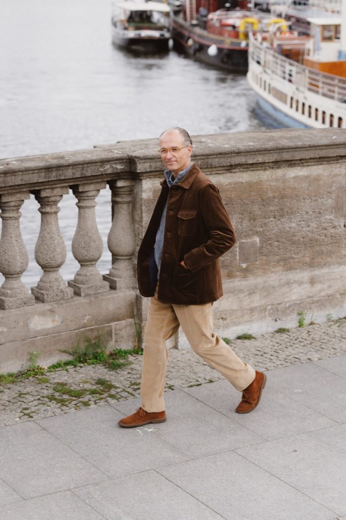 Kord-Sakkojacke von Beaver’s Fulham im Gehen an der Uferbalustrade, dahinter die Ausflugsschiffe