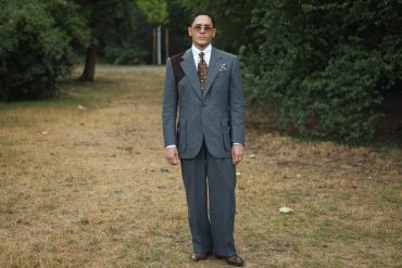 Yasin Tarabia in einem graublauen Anzug mit weiter Hose, ganze Figur in einem Wiener Park
