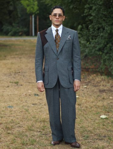 Yasin Tarabia in einem graublauen Anzug mit weiter Hose, ganze Figur in einem Wiener Park