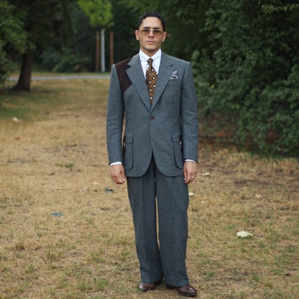 Yasin Tarabia in einem graublauen Anzug mit weiter Hose, ganze Figur in einem Wiener Park