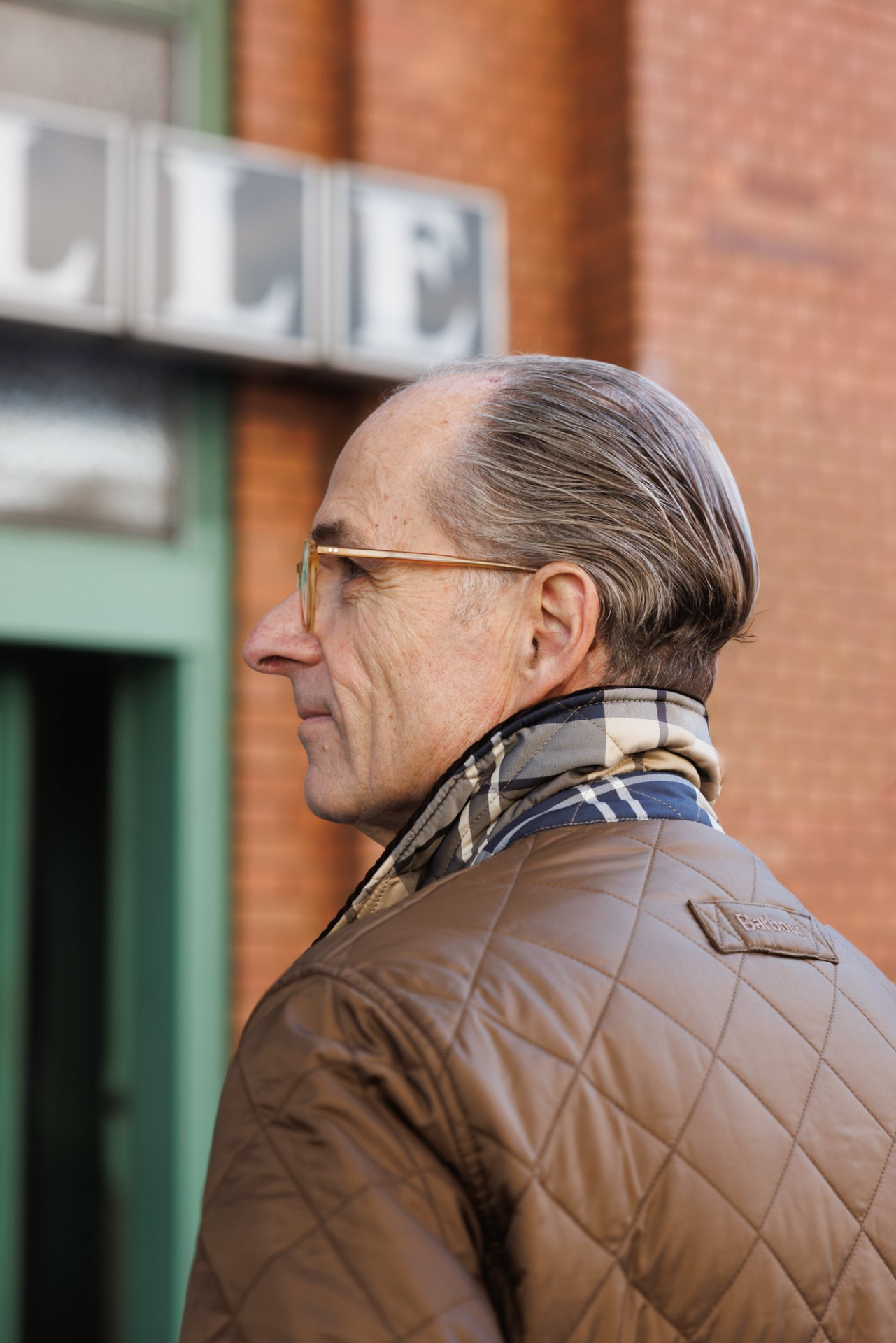 Bernhard Roetzel im Profil, Steppjacke mit Karoschal vor der Backsteinfassade der Markthalle