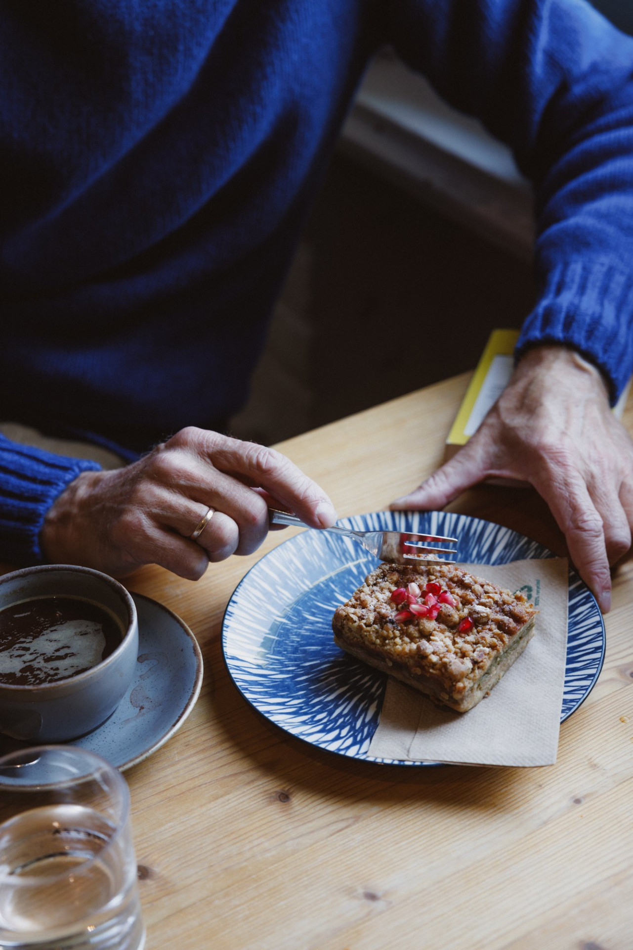Hände über einem Teller mit Kuchen, daneben ein Kaffee, Bernhard Roetzel im blauen Turtleneck