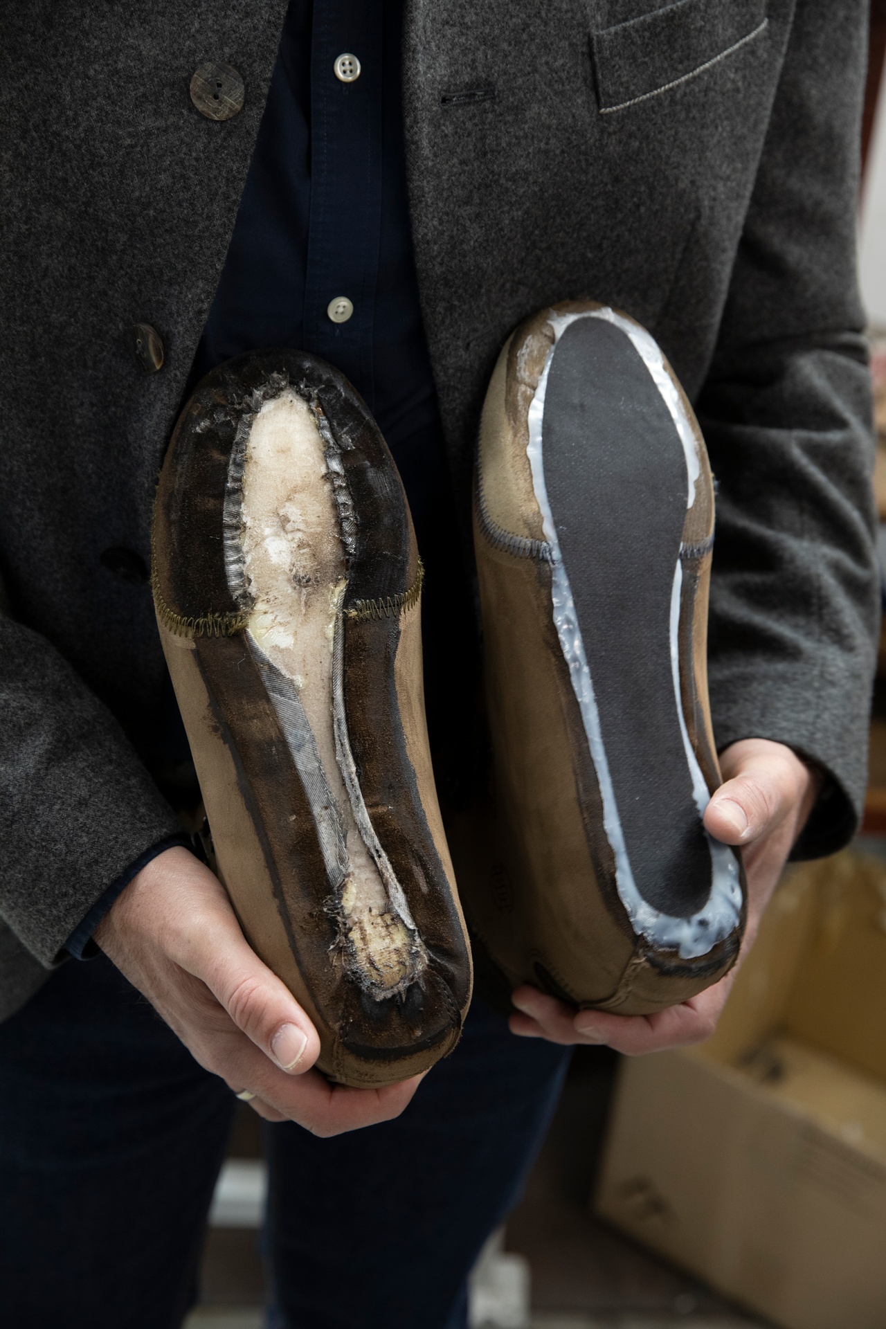 Zwei Schuhsohlen von unten, gehalten von einem Mann im grauen Sakko