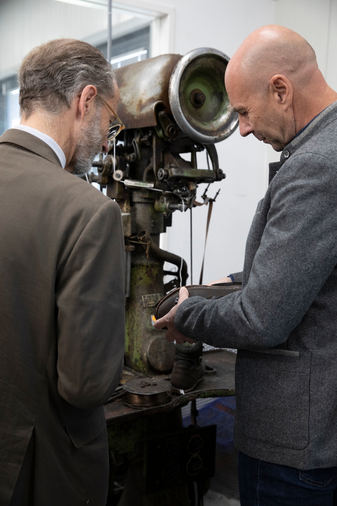 Bernhard Roetzel und Thomas Gröger stehen an einer alten Maschine, Gröger hält einen Schuh in der Hand