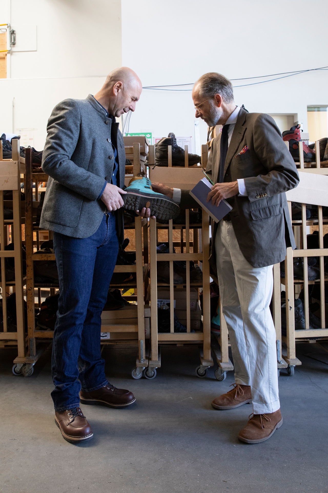 Bernhard Roetzel und Thomas Gröger stehen vor Regalen mit Schuhen und halten einen Schuh in der Hand