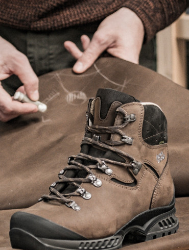 Brauner Hanwag-Bergstiefel auf einer Lederhaut, darüber zeichnet ein Mitarbeiter mit Kreide an