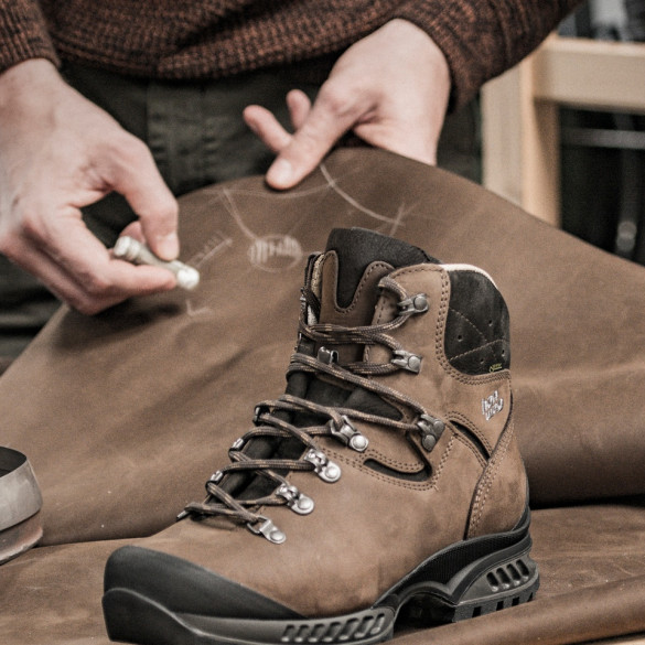 Brauner Hanwag-Bergstiefel auf einer Lederhaut, darüber zeichnet ein Mitarbeiter mit Kreide an