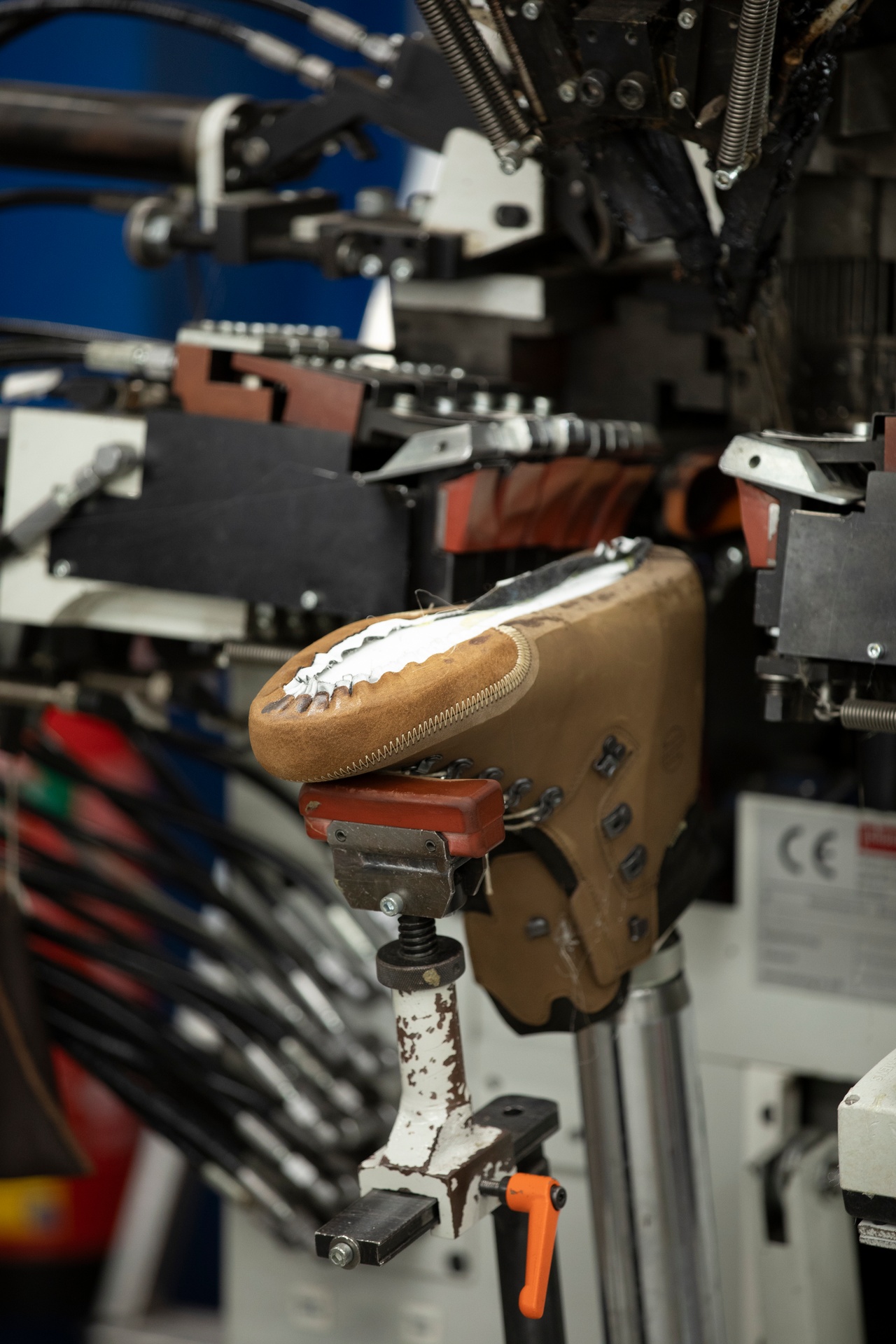 Ein Schuh sitzt auf dem Leisten in einer Maschine, im Hintergrund weitere Maschinenteile