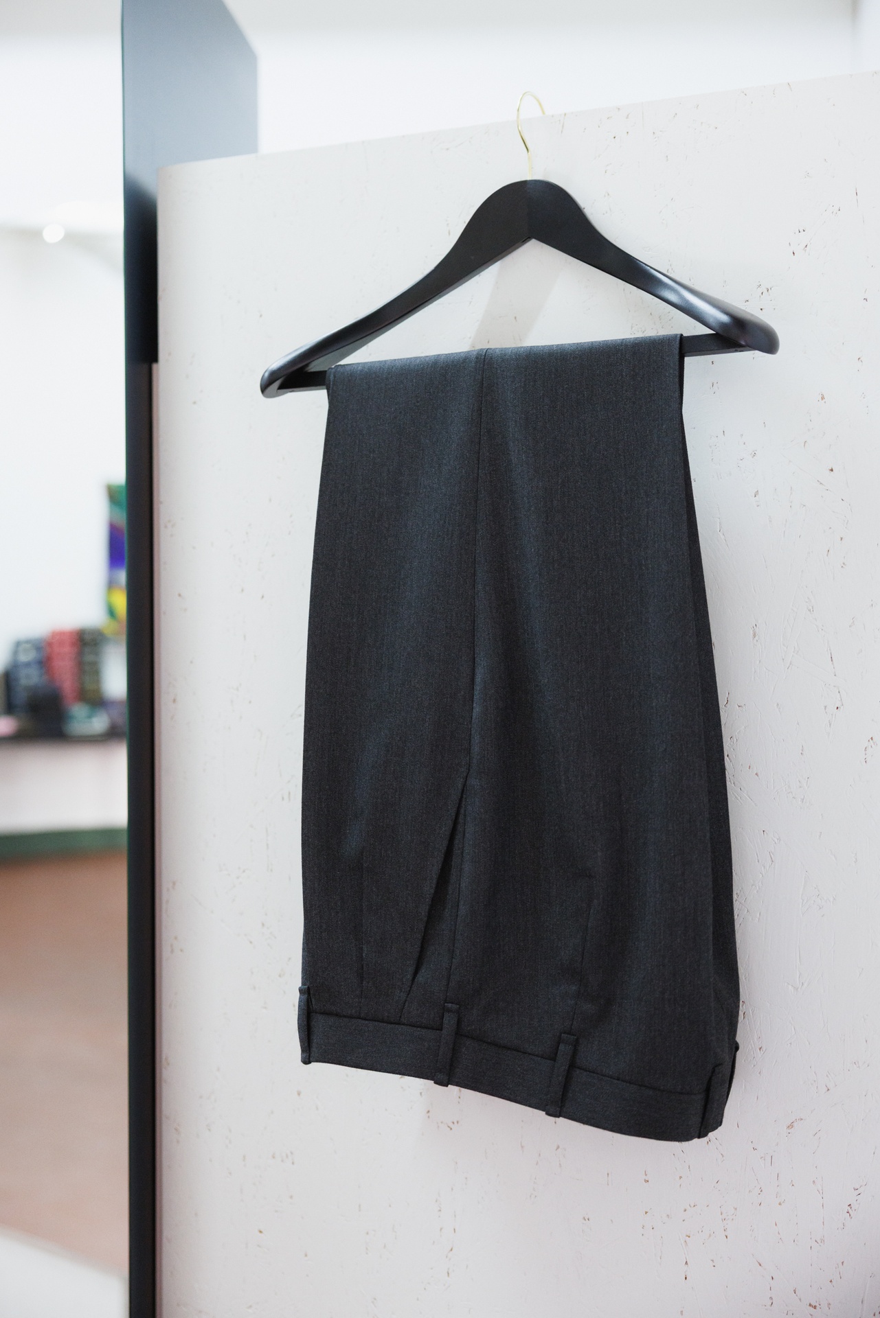 Eine dunkelgraue Hose mit Umschlag hängt am Bügel an einer weißen Wand